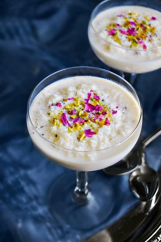 A martini glass with vegan coconut rice pudding and garnish on a dark blue backdrop