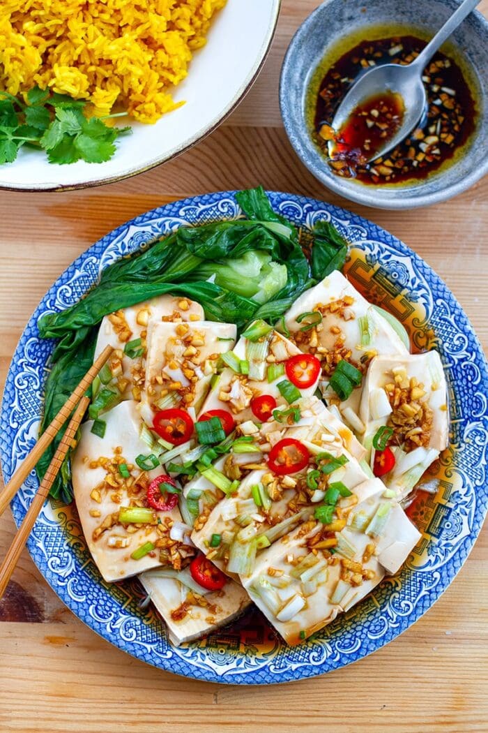 A blue-trimmed plate holding large slices of tofu and pieces of bok choy with seasoning