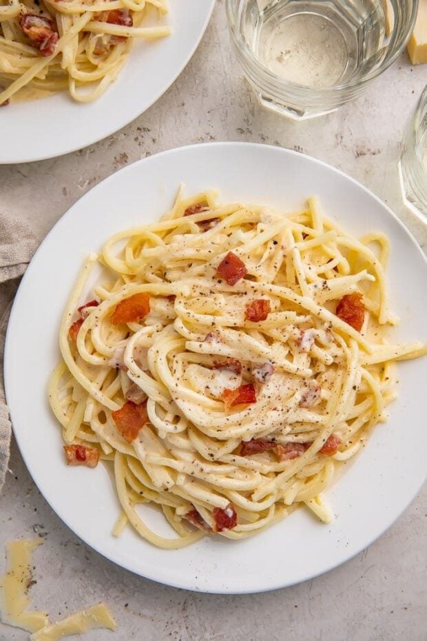 A full white plate of keto carbonara on a white tablecloth next to a glass of water