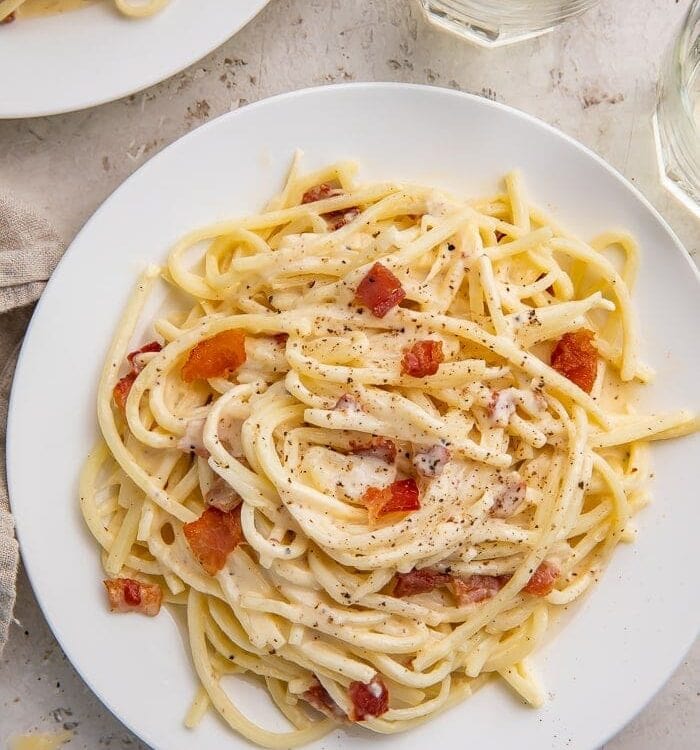 A full white plate of keto carbonara on a white tablecloth next to a glass of water