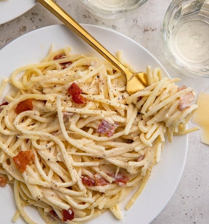 A white plate of keto carbonara with a golden fork