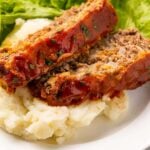 Two slices of keto meatloaf plated on mashed cauliflower with a romaine lettuce garnish