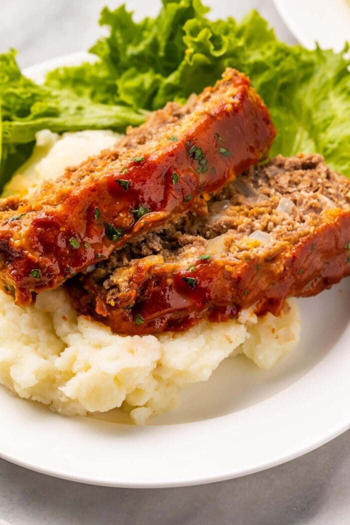 Two slices of keto meatloaf plated on mashed cauliflower with a romaine lettuce garnish