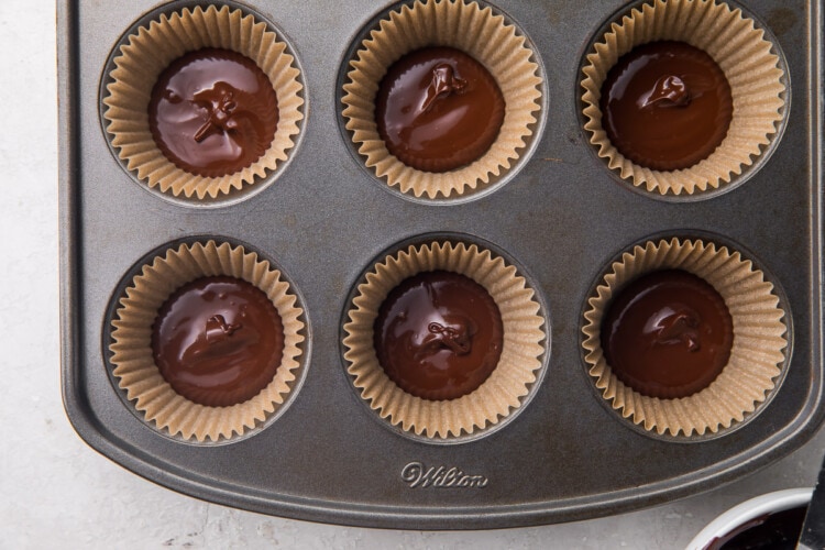 Bottom layer of melted chocolate in 6 cupcake liners in a metal cupcake pan.