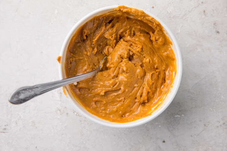 White mixing bowl holding peanut butter and powdered erythritol mixture with a silver spoon.