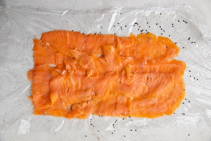 Thinly sliced salmon arranged in a large rectangle on a sheet of plastic wrap