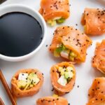 8 pieces of keto smoked salmon sushi on a white plate with chopsticks next to a bowl of soy sauce