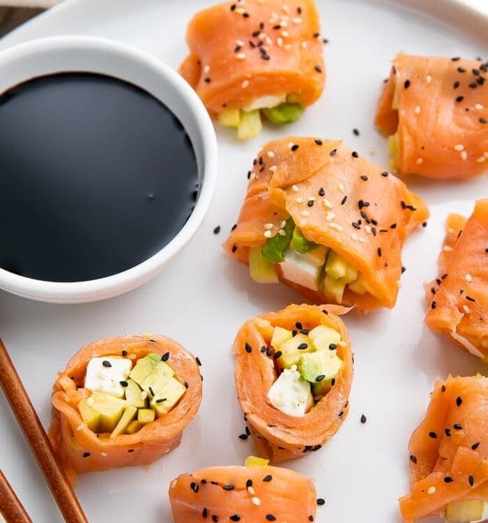 8 pieces of keto smoked salmon sushi on a white plate with chopsticks next to a bowl of soy sauce