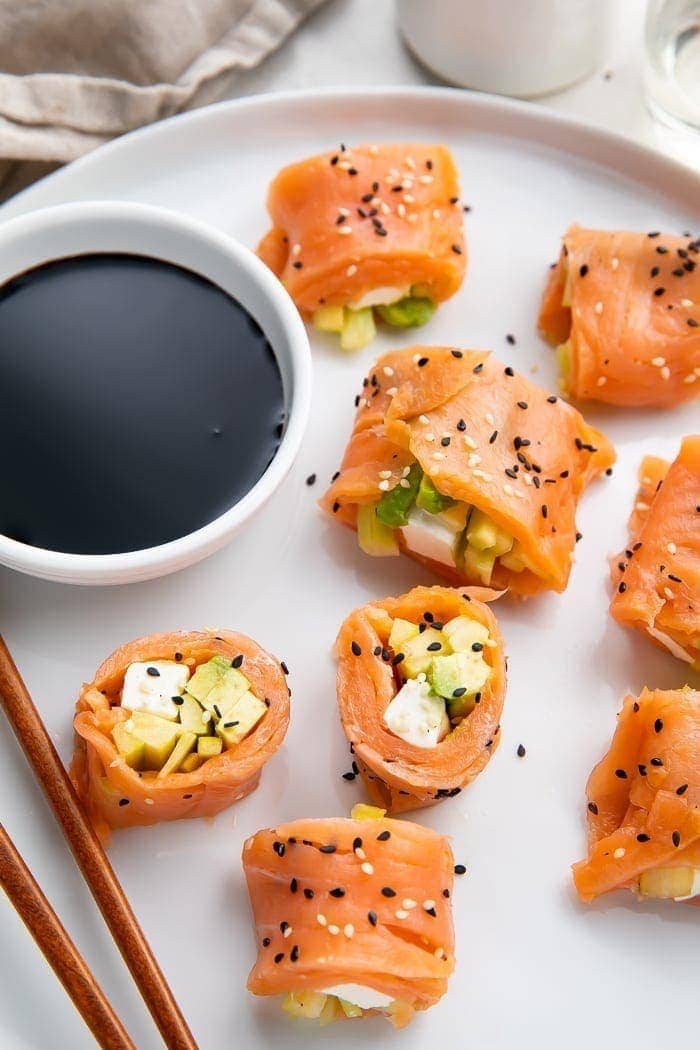 8 pieces of keto smoked salmon sushi on a white plate with chopsticks next to a bowl of soy sauce