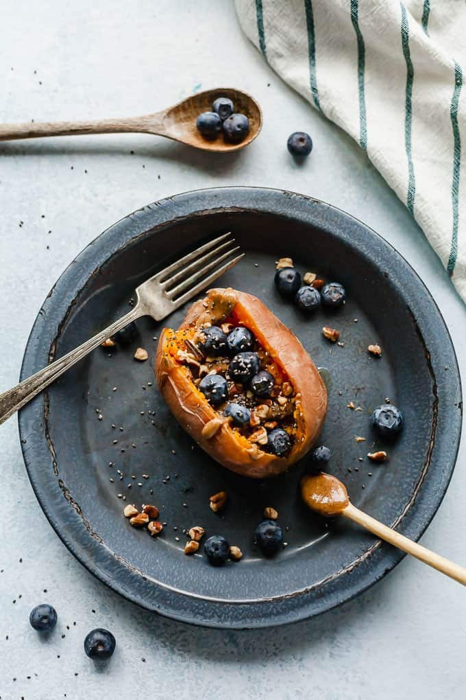 Breakfast stuffed sweet potato on a grey-blue plate with a fork and blueberries