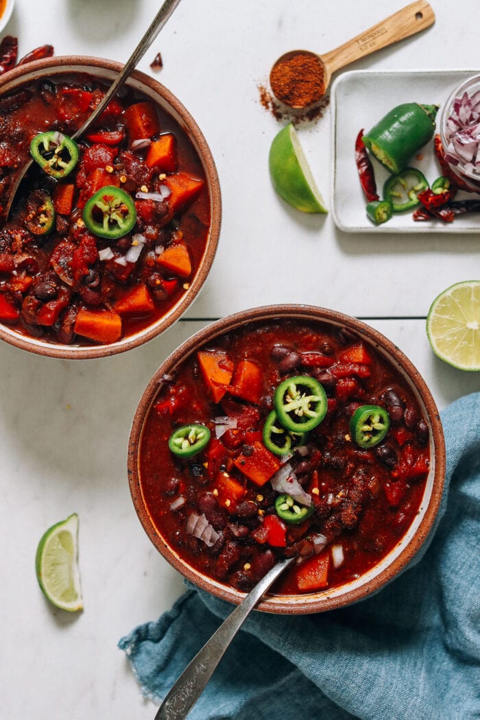 Two brown bowls holding deep red vegan chili with jalapeños and a silver spoon