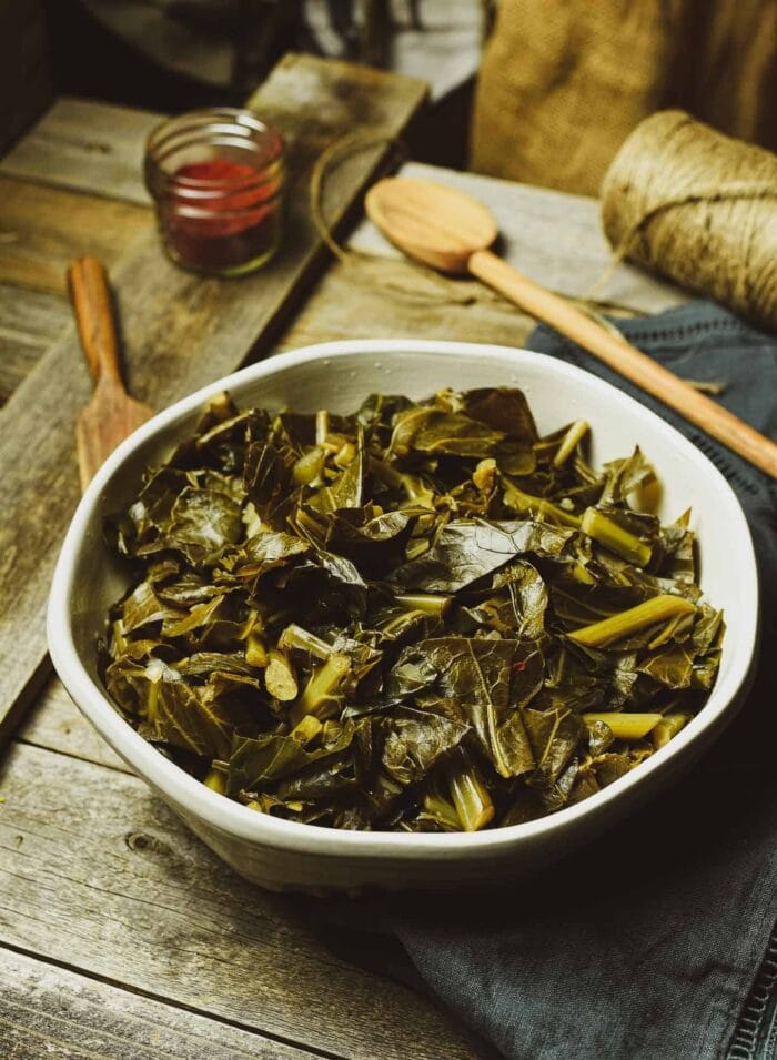 Vegan Instant Pot collard greens in a funky sage bowl with a wooden spoon on a wooden table