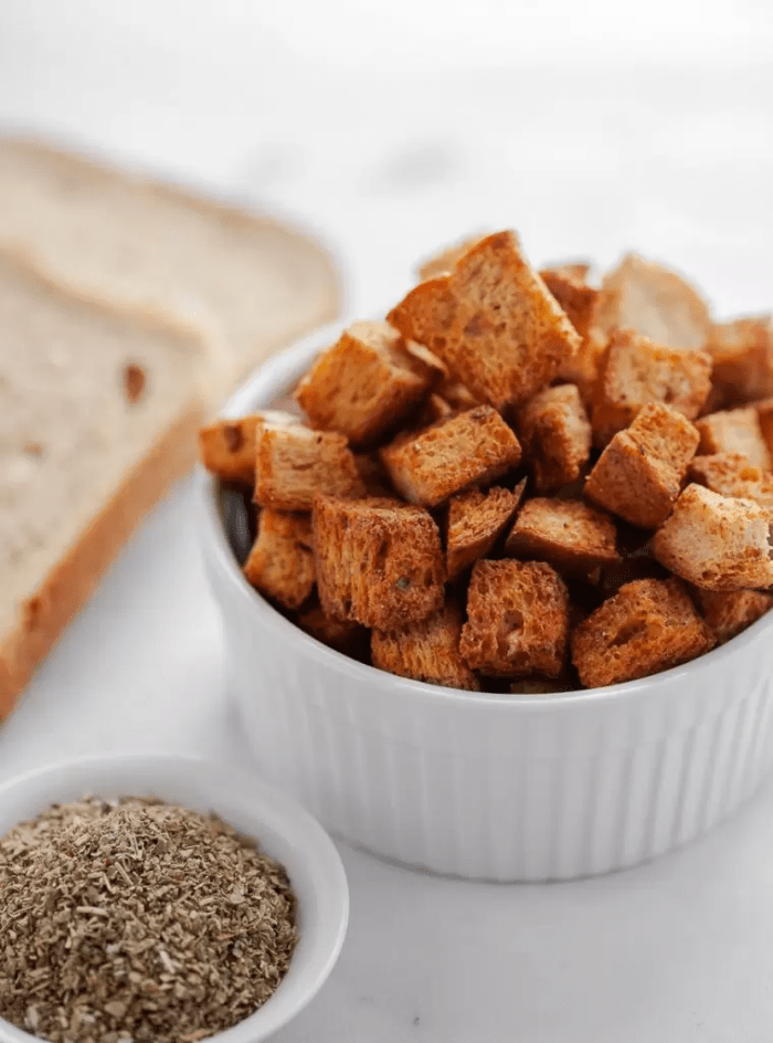 A white bowl of air fried croutons next to a slice of keto bread