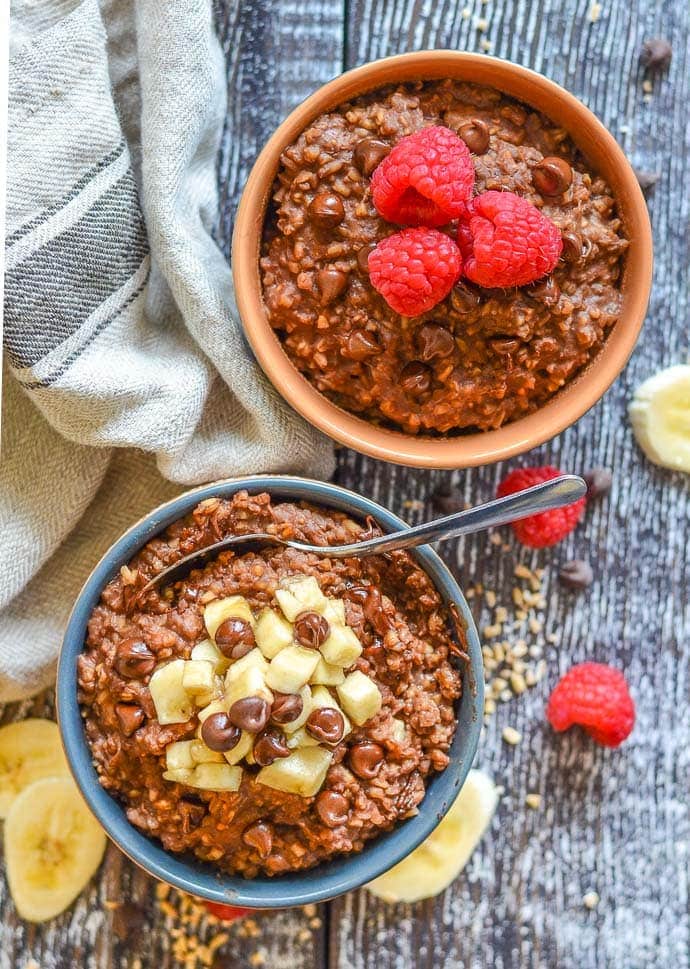 Two bowls of chocolate steel cut oats, one topped with bananas, one topped with raspberries
