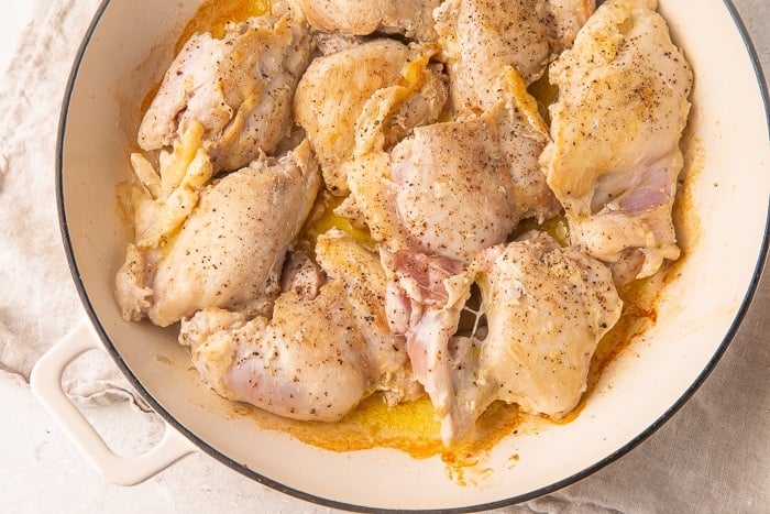 Heavy sauté pan full of chicken thighs in olive oil