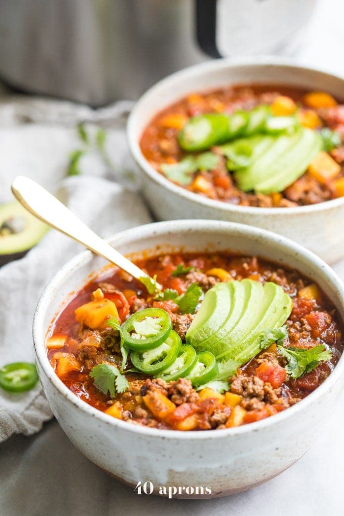 Two white bowls of butternut squash chili garnished with avocado in front of an Instant Pot