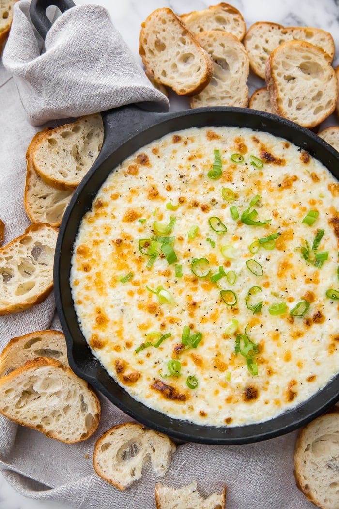 Hot crab dip in a cast iron skillet surrounded by crostini