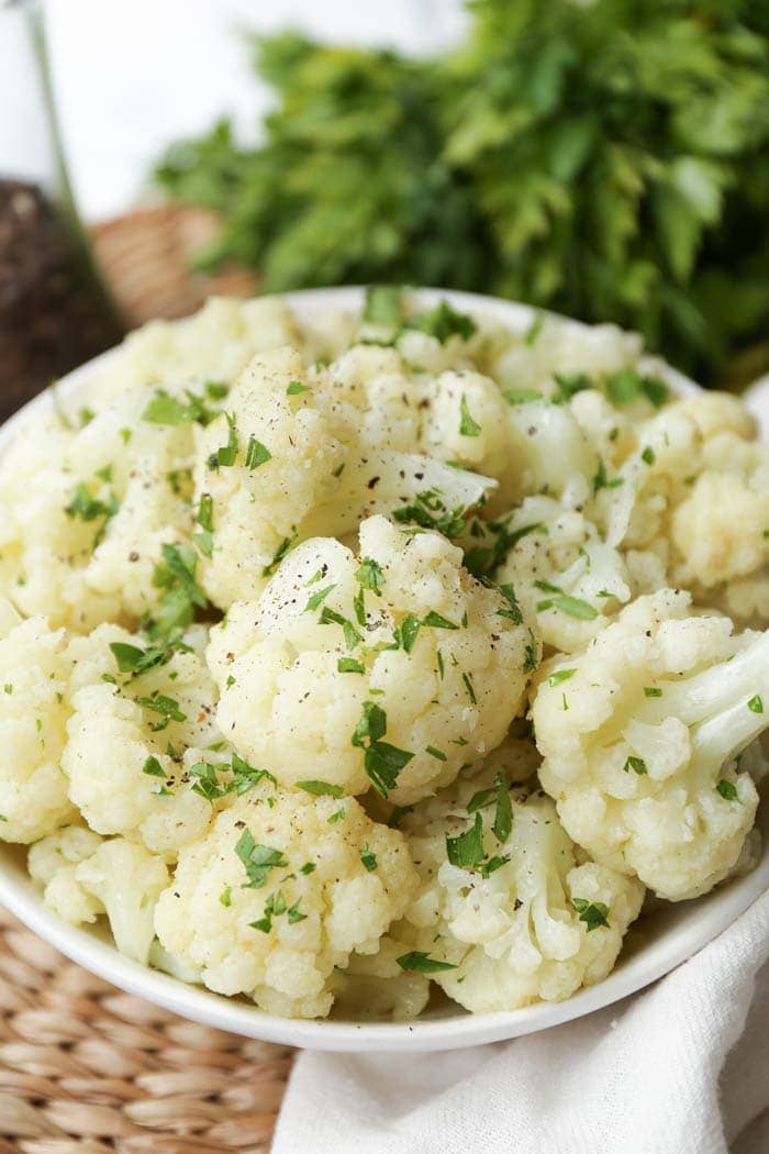 Close up view of cauliflower in a white bowl with green garnish