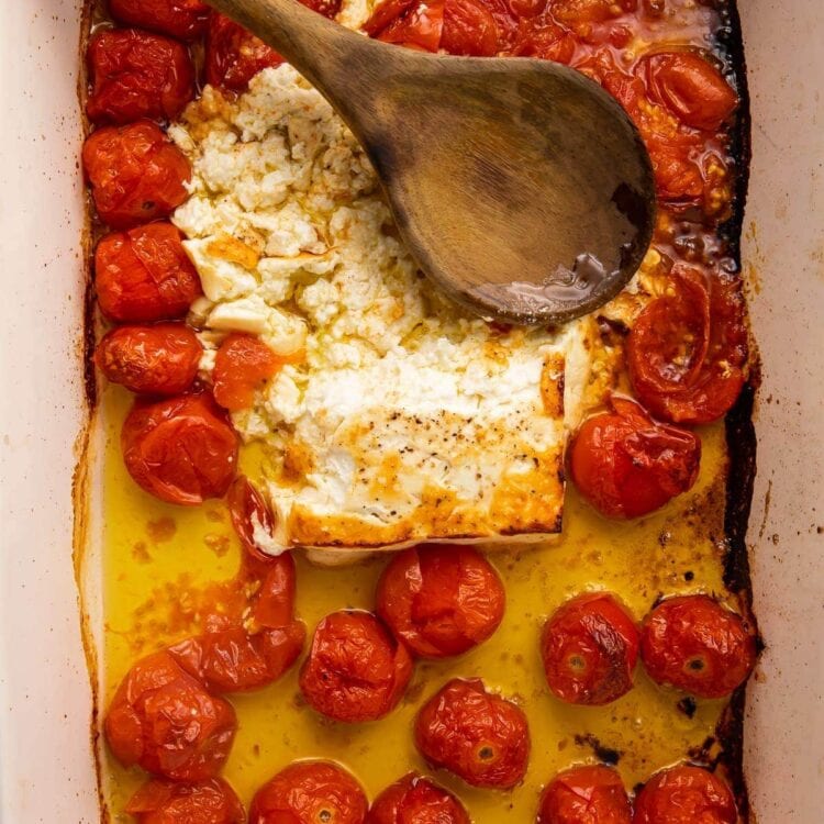 Baked feta and tomatoes smushed in oil in a large pan with a wooden spoon