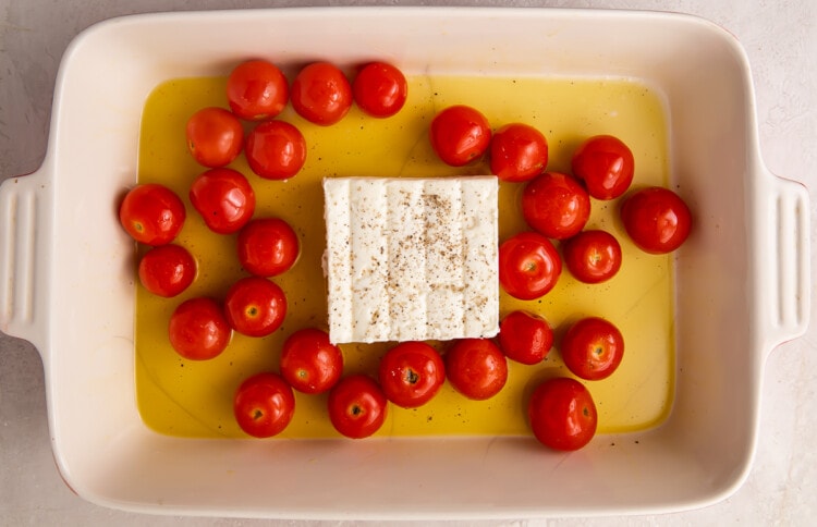 Cherry tomatoes and feta in a pool of olive oil in a rectangular baking dish