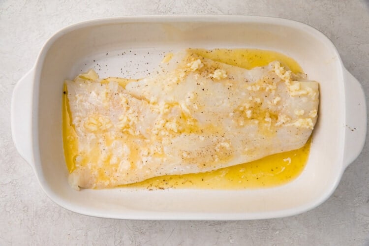 Uncooked fish in a baking dish, covered with lemon-garlic butter