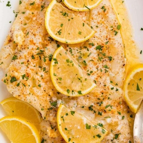 Baked fish with lemon garlic butter sauce and slices of lemon on a white platter