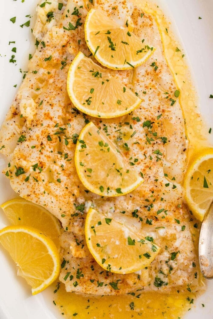 Baked fish with lemon garlic butter sauce and slices of lemon on a white platter
