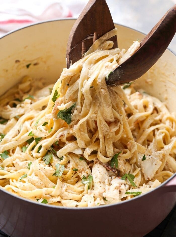 A pot of crab alfredo, with a scoop being lifted out with tongs