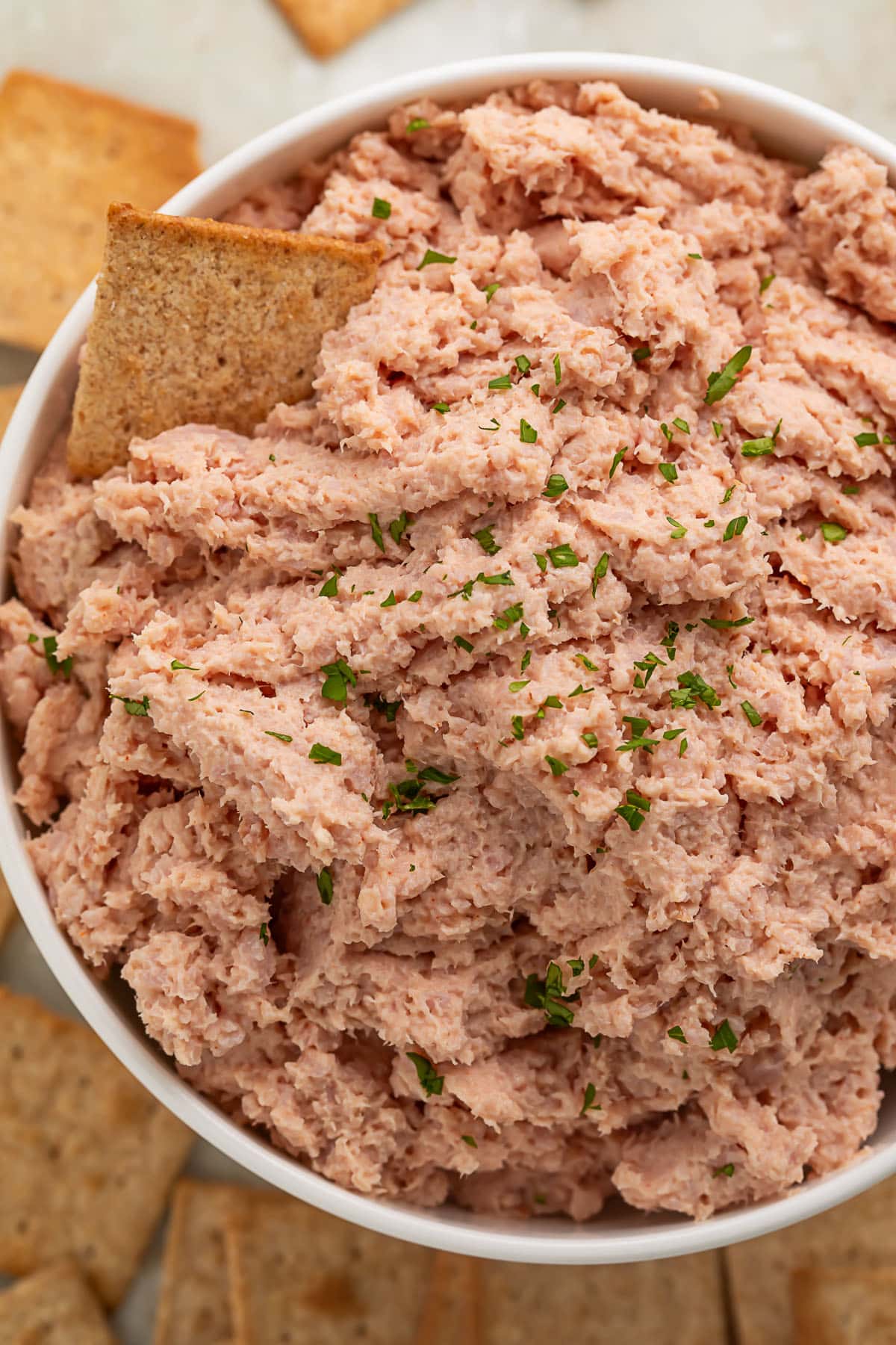 Overhead photo of a large bowl of deviled ham with a square wheat cracker resting in the dip.