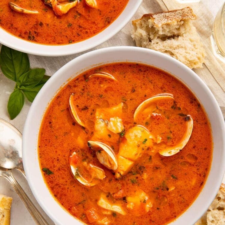 Two bowls of red Italian fish stew on a table surrounded by pieces of bread