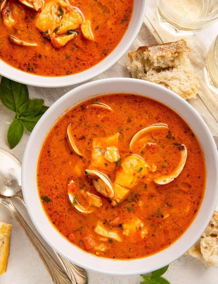 Two bowls of red Italian fish stew on a table surrounded by pieces of bread