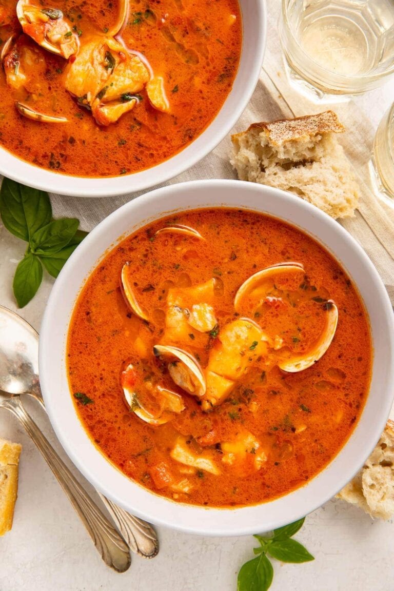 Two bowls of red Italian fish stew on a table surrounded by pieces of bread