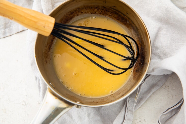 Lemon butter sauce in a silver saucepan with a black whisk
