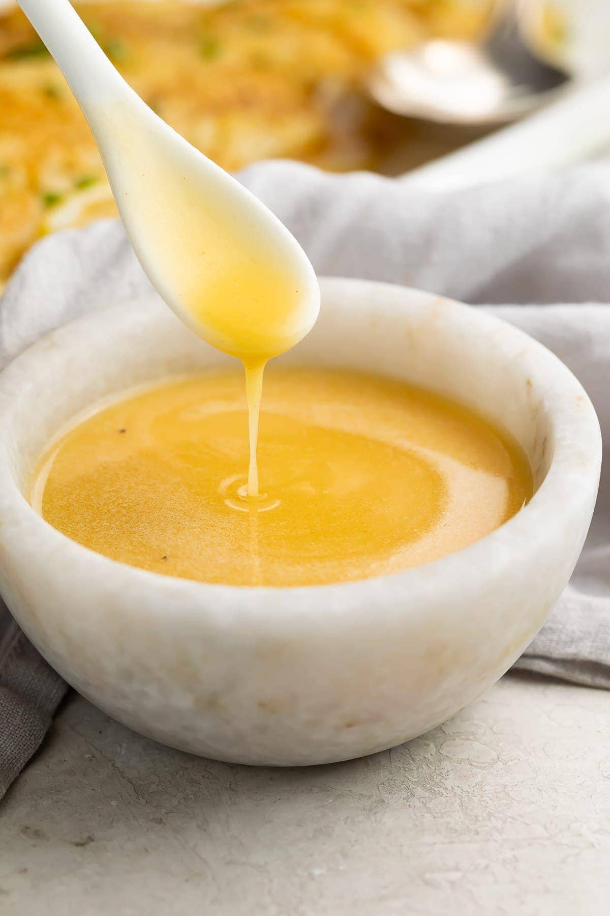 A spoon drizzling lemon butter sauce into a stone bowl