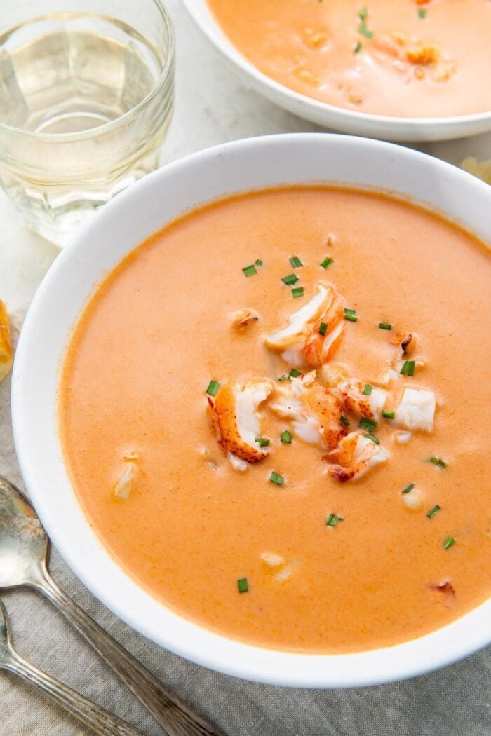 A large white bowl full of orange bisque with chunks of lobster, taken from an overhead angle