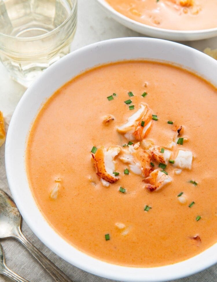 A large white bowl full of orange bisque with chunks of lobster, taken from an overhead angle