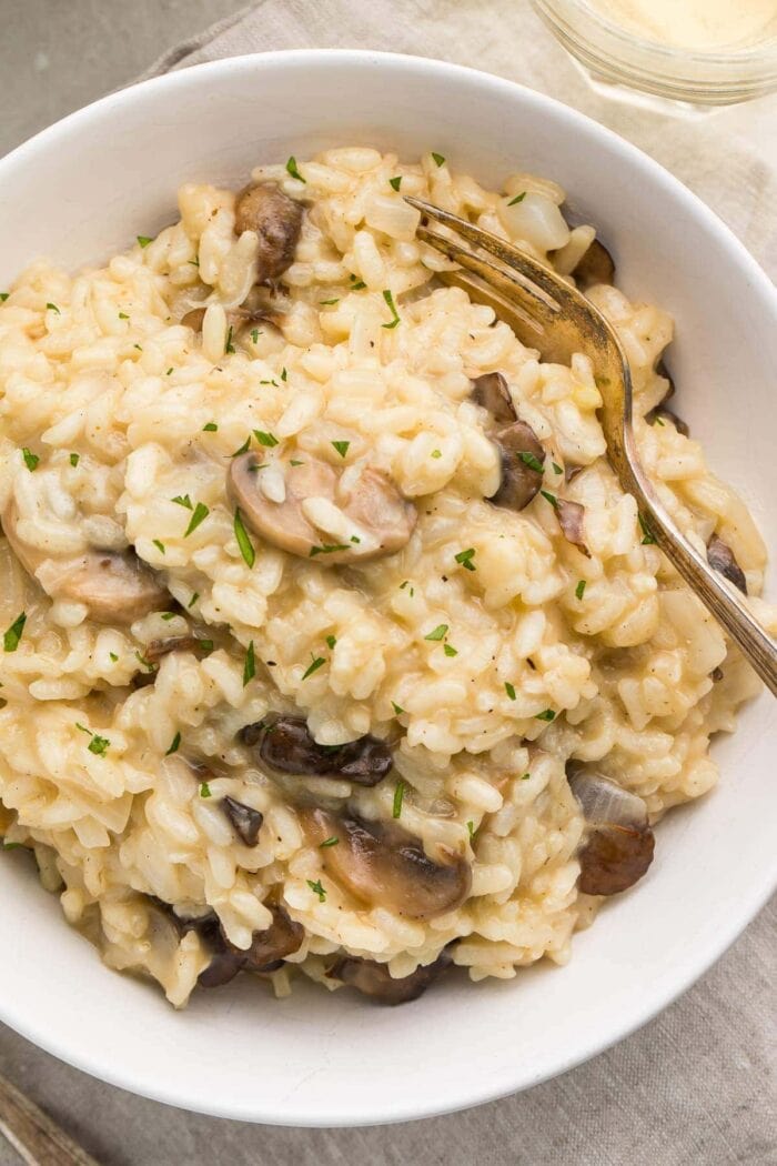 Close up photo of a white bowl with mushroom risotto and a gold fork