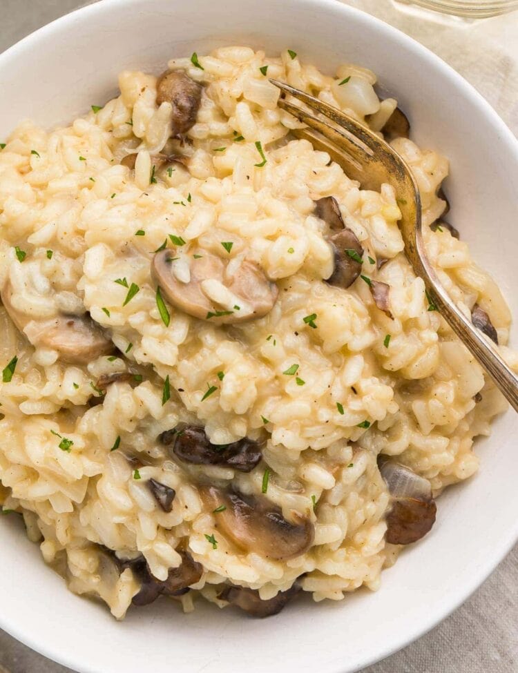 Close up photo of a white bowl with mushroom risotto and a gold fork