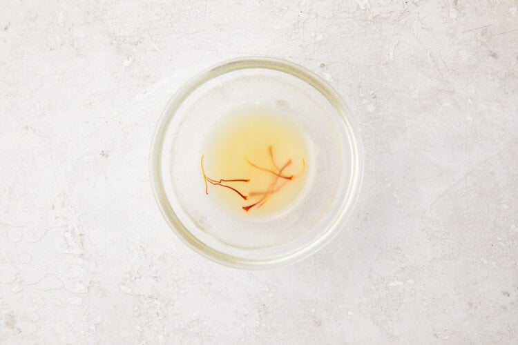 A small glass bowl containing chicken stock and saffron threads for seasoning mushroom risotto
