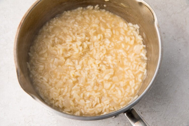 Risotto rice with chicken stock in a large silver saucepan