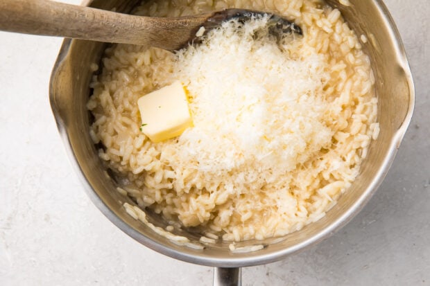 Risotto, parmesan, and butter in a large silver saucepan with a wooden spoon