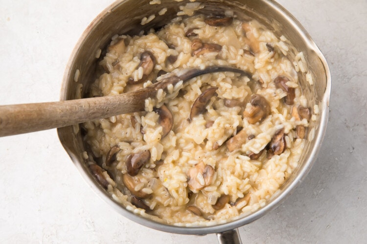 Mushrooms stirred into a large silver saucepan of risotto with a wooden spoon