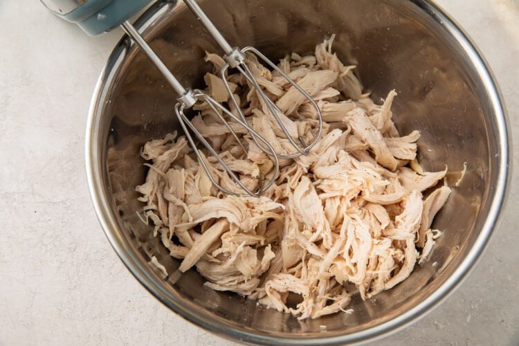 Chicken breast shredded using a hand mixer in a large silver bowl