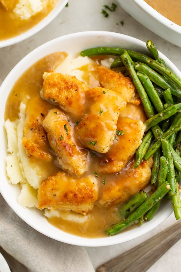 Whole30 fried chicken and gravy on a bed of mashed potatoes, served in a bowl with tender-crisp green beans.