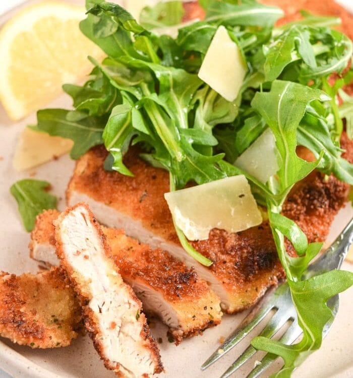Chicken Milanese topped with arugula on a tan plate