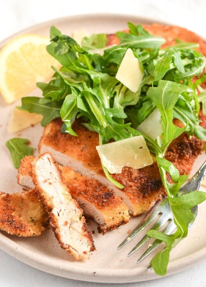 Chicken Milanese topped with arugula on a tan plate