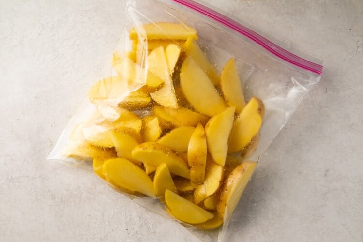 Raw potato wedges and olive oil in a plastic bag