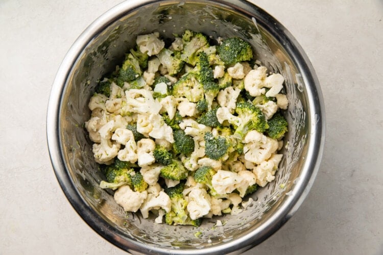 Broccoli and cauliflower florets in a large mixing bowl with dressing.