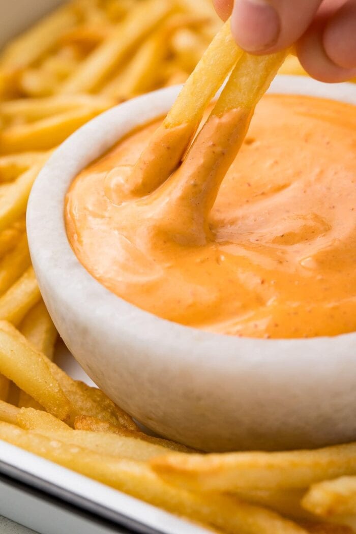 Two french fries dipped in chipotle aioli in a small bowl