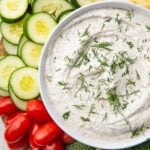 A bowl of dill dip surrounded by veggies